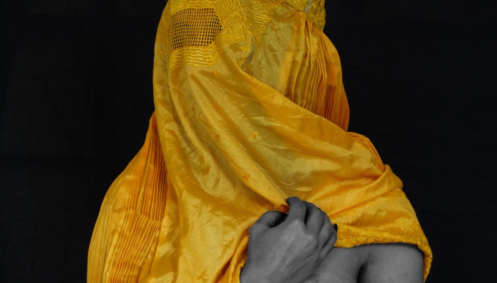 A women in a yellow Burqa looking left and exposing one of her breasts.